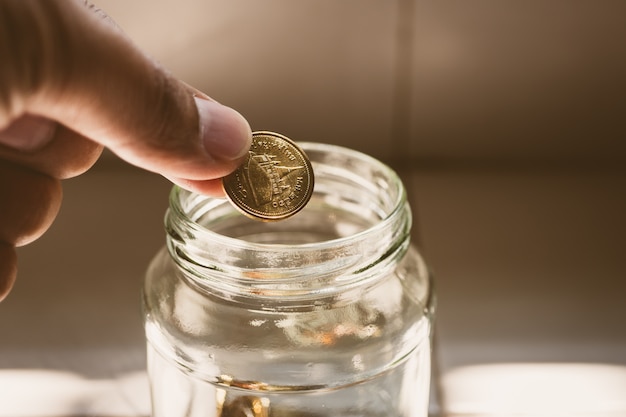 Closeup main mettre des pièces de monnaie dans un bocal en verre utilisant comme concept d&#39;épargne financière et de l&#39;argent