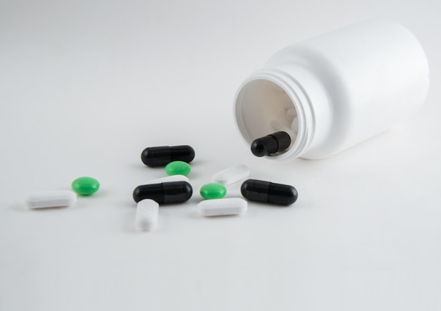 Closeup pilules et bouteille de pilules à verser sur fond blanc.