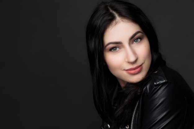 Closeup portrait de belle femme modèle brunnette souriant pour la caméra tout en posant isolé sur fond noir en studio.