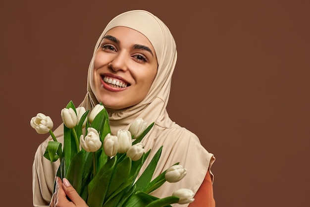 Closeup portrait belle femme musulmane portant le hijab beige souriant tenant un gros bouquet de tulipes