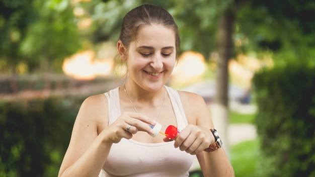 Closeup portrait de belle jeune femme souriante soufflant des bulles de savon dans le parc au coucher du soleil