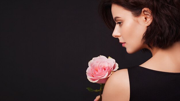 Closeup portrait d'une belle jeune femme tenant une rose rose