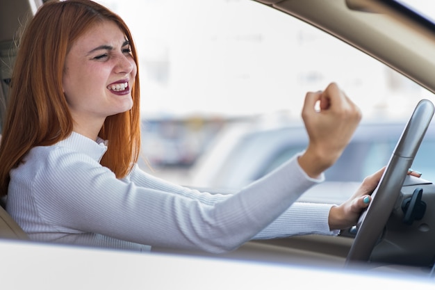 Closeup portrait de femme agressive en colère mécontente au volant d'une voiture en criant à quelqu'un avec le poing vers le haut.