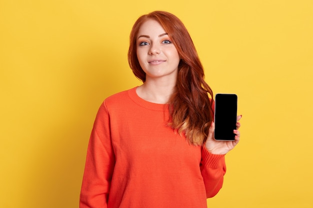 Closeup portrait de femme aux cheveux rouges tenant un téléphone intelligent avec écran noir dans les mains