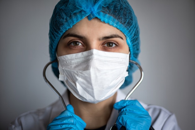 Closeup portrait d'une femme médecin portant un masque stérile médical. Infirmière à l'écoute du stéthoscope et à la caméra. Concept de test de maladie de la grippe coronavirus. Le travailleur hospitalier sert le patient.