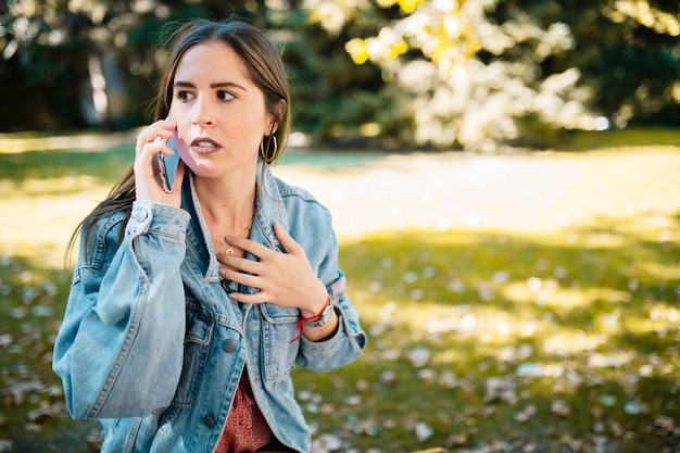 Closeup portrait de femme stressée tenant un téléphone portable inquiet a reçu de mauvaises nouvelles dans le parc de la ville. Émotion humaine expression du visage, sentiment, langage corporel de réaction. Femme avec la main ouverte sur la poitrine inquiète.