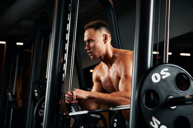 Closeup portrait d'un homme musclé entraînement avec haltères au gymnase. Homme athlétique bodybuilder brutal avec six packs, abdominaux parfaits, épaules, biceps, triceps et poitrine.