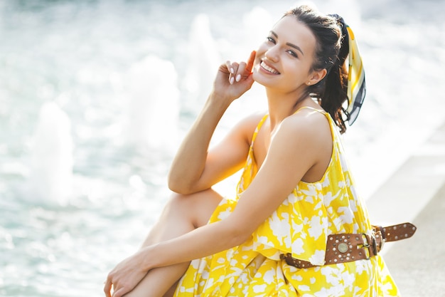 Closeup portrait de jeune femme séduisante en robe jaune. Loisirs d'été. Belle femme élégante marchant dans la ville. Femme près de la fontaine.