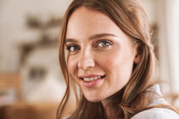 Closeup portrait de jeune femme souriante joyeuse belle rousse à l'intérieur à la maison.