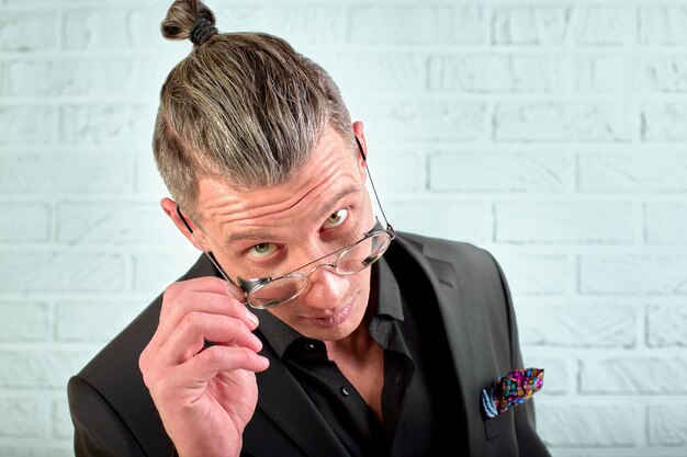 Closeup portrait d'un jeune homme d'affaires heureux avec des lunettes en regardant la caméra sur le mur blanc