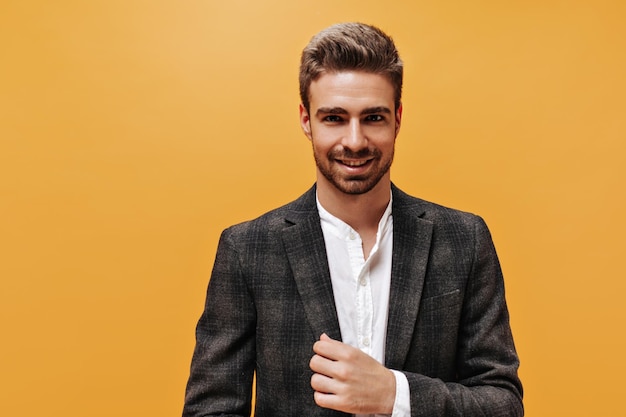 Closeup portrait de jeune homme barbu en veste à carreaux et chemise blanche sur fond orange Jeune homme en costume élégant sourit sur isolé