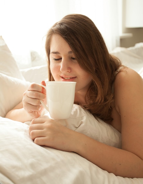 Closeup portrait de jolie femme buvant du café au lit