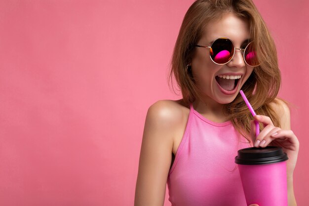 Closeup portrait de jolie jeune femme blonde positive portant haut rose et lunettes de soleil colorées