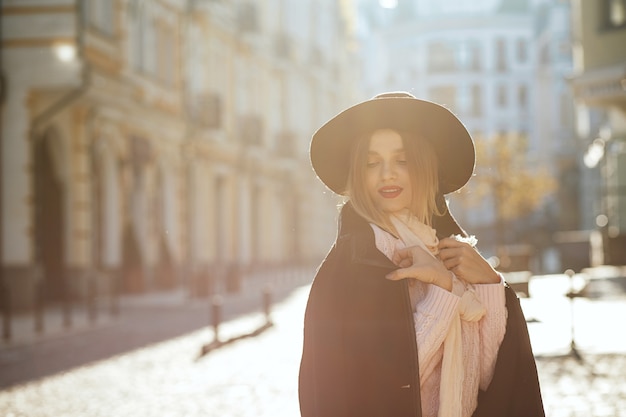 Closeup portrait de mannequin blonde glamour portant chapeau et manteau posant avec la lumière du soleil. Espace pour le texte