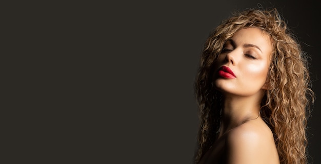 Closeup portrait de mode d'une jeune femme sensuelle avec des lèvres rouges et des cheveux bouclés posant sur le mur gris. Espace libre