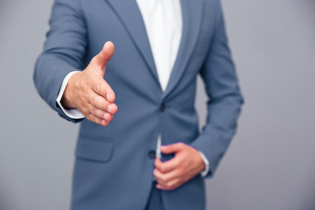 Closeup portrait of a businessman stretching main pour poignée de main sur mur gris