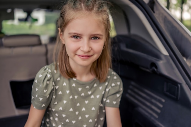 Closeup portrait of cute preteen girl with belle coiffure assis dans le coffre de la voiture et souriant en regardant la caméra. Enfant heureux dans le véhicule à la nature pendant le voyage d'été