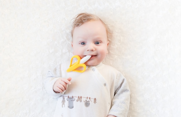 Closeup portrait petit garçon mignon avec de grands yeux bleus avec un jouet dans ses mains, mordille un jouet de dentition banane