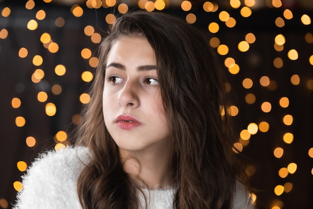 Closeup portrait de très belle jeune femme sur fond de lumières de Noël bokeh. Portrait féminin attrayant à l'intérieur. Portrait de jolie femme avec des guirlandes chaudes vacances festives