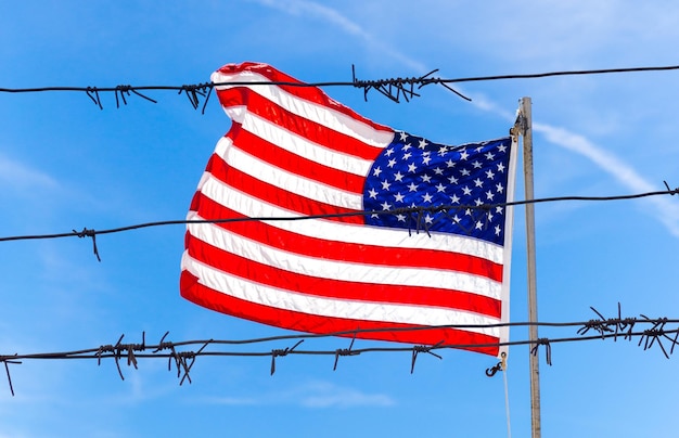 Clôture de barbelés devant le drapeau des États-Unis d'Amérique agitant dans le vent avec fond de ciel bleu