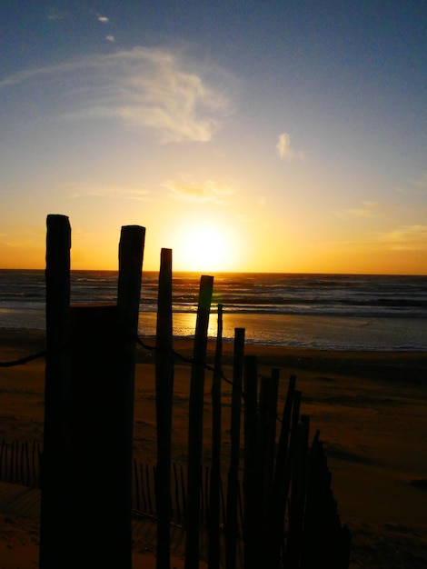 Une clôture en bois sur la plage contre le ciel au coucher du soleil.