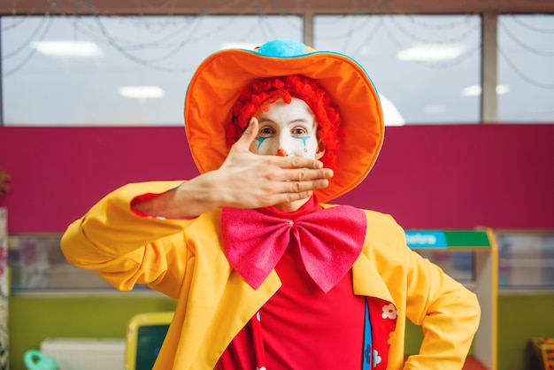 Un clown drôle montre des tours avec des expressions faciales dans la zone des enfants. Fête d'anniversaire dans la salle de jeux, vacances de bébé dans l'aire de jeux. Bonheur d'enfance, loisirs enfantins, divertissement avec animateur