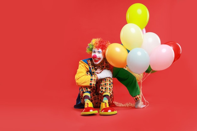 Clown heureux avec des ballons colorés sur fond rouge pour le texte