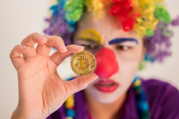 Clown pleurant tenant la pièce de Bitcoin, concept de tromperie ou de perte d'investissement
