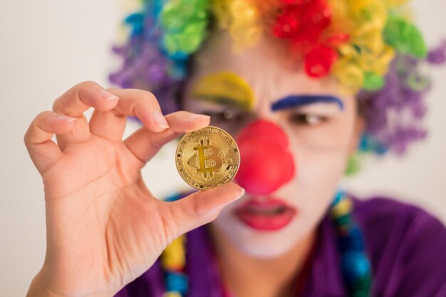 Clown pleurant tenant la pièce de Bitcoin, concept de tromperie ou de perte d&#39;investissement