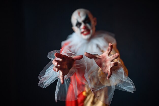 Clown Sanglant Fou Atteignant La Victime Avec Ses Mains, Vue De Face. Homme Avec Du Maquillage En Costume De Carnaval, Fou Maniaque