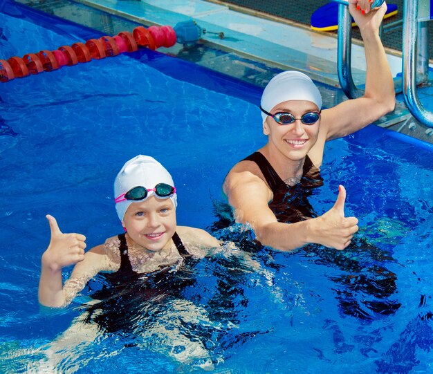 Coach charmant avec son élève nageant dans la piscine et souriant