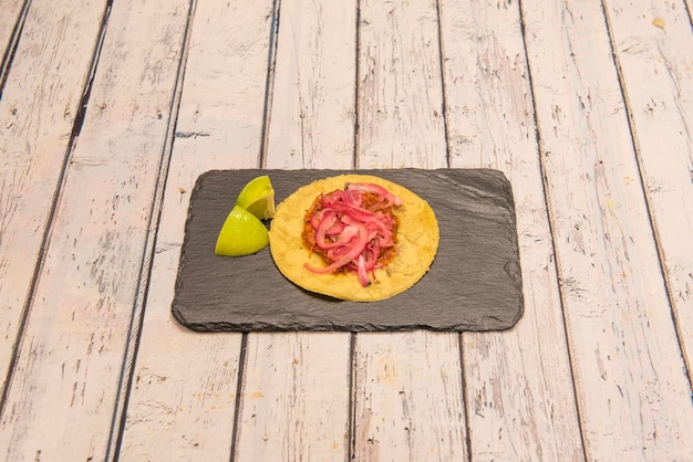 Cochinita pibil taco sur tortilla de maïs et quartiers de citron vert sur plaque d'ardoise noire