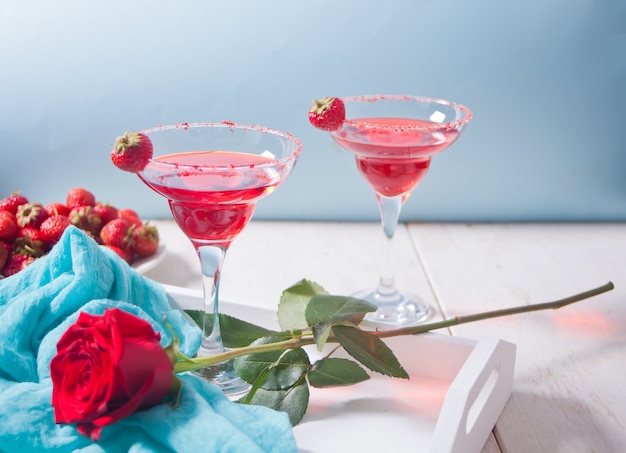 Cocktail alcoolique exotique rouge dans des verres clairs et rose rouge sur le plateau blanc en bois pour un dîner romantique.