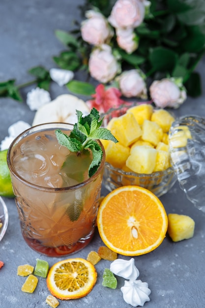 Cocktail d'ananas rafraîchissant froid au citron vert et à la menthe pour une chaude journée d'été sur une surface grise décorée de fruits confits à la menthe et aux cubes d'ananas idée de mojito limonade maison avec des glaçons