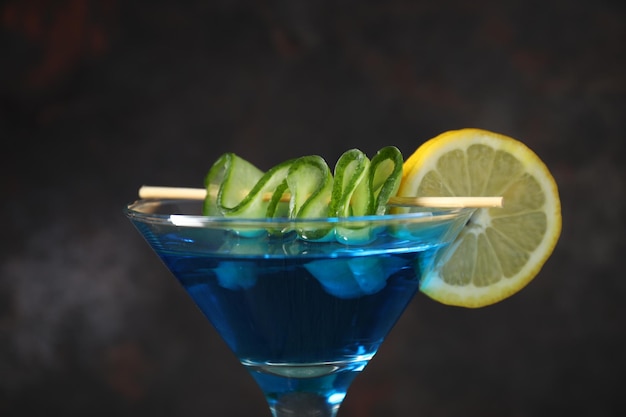 Cocktail bleu avec des tranches de citron et de concombre dans le verre sur fond gris foncé en gros plan