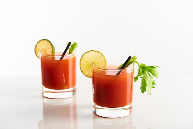 Cocktail Bloody Mary dans des verres garnis de citron vert et de céleri isolé sur blanc