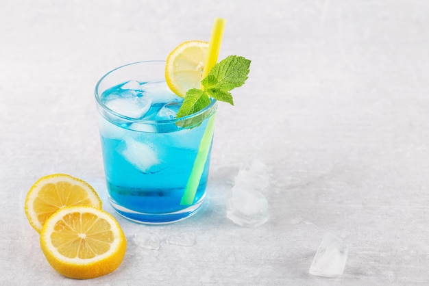 Cocktail Blue Lagoon sur table gris clair avec citron et menthe