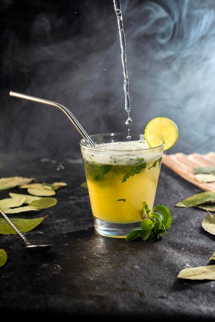 Photo cocktail ou boisson versant dans un verre en verre avec des feuilles et du citron et des fumées