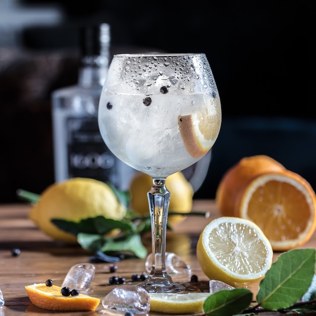 Un cocktail de citron froid avec des tranches de glace est sur la table avec des citrons entiers et des oranges