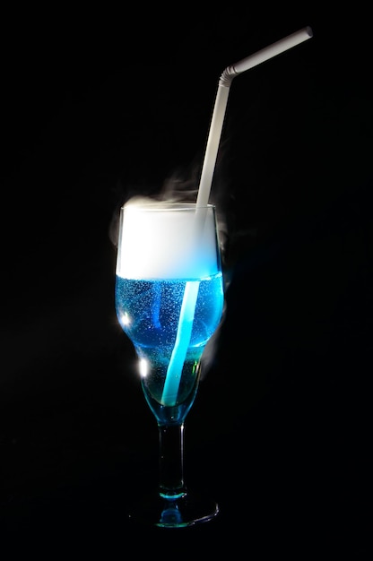 Cocktail curaçao bleu avec sambuca. Paille blanche dans un verre sur fond noir