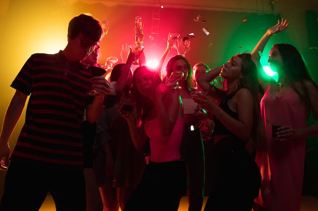 Cocktail. Une foule de personnes en silhouette lève les mains, dansant sur une piste de danse sur fond néon. Vie nocturne, club, musique, danse, mouvement, jeunesse. Des couleurs vives et des filles et des garçons émouvants.