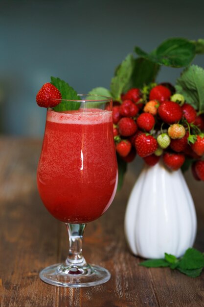 Cocktail de fraises en verre embué et vase en céramique blanche avec des branches de fraises rouges mûres