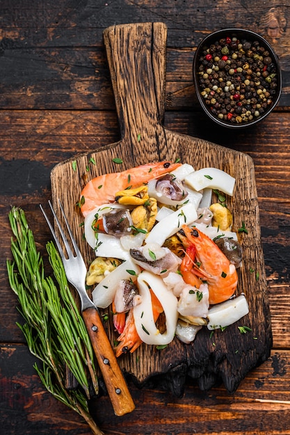 Cocktail de fruits de mer crus avec crevettes, crevettes, moules, calamars et poulpes sur une planche à découper. Fond en bois foncé. Vue de dessus.