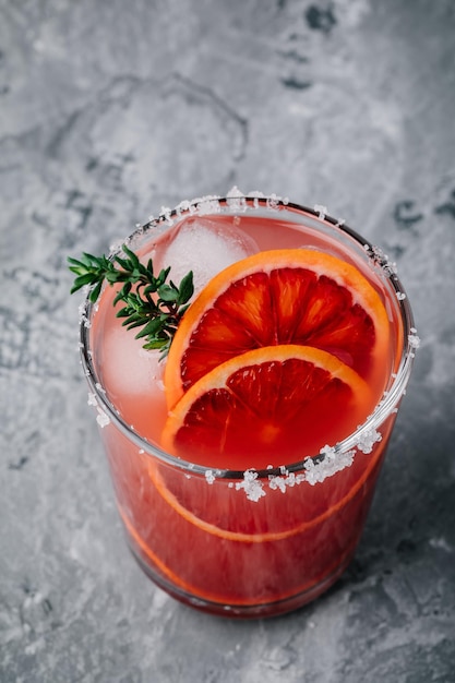 Cocktail de gin de fleur de sureau à l'orange sanguine avec de la glace et du thym sur fond sombre