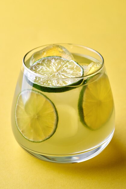 Cocktail de gin tonic soda garni d'une tranche de citron sur fond jaune.