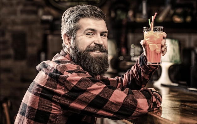 Cocktail homme barbu. Homme de portrait, buvant du jus d'orange. Barman dans un pub ou un restaurant. Homme barbu gai, boire des cocktails et sourire. Cocktail frais alcoolisé tropical.