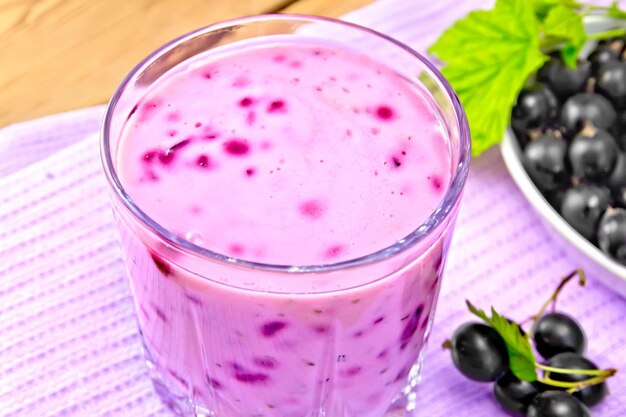 Cocktail de lait au cassis dans un verre sur une serviette, soucoupe aux baies sur fond de planche de bois