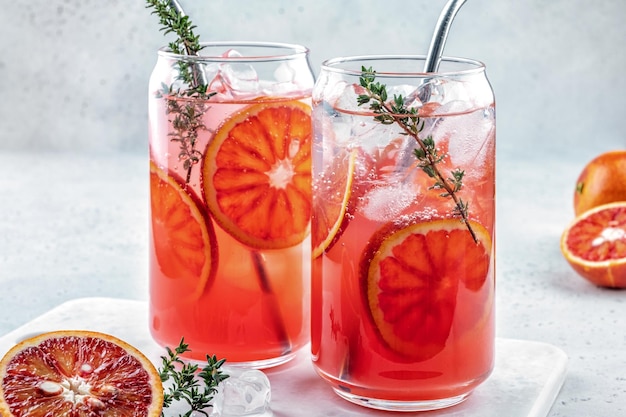 Cocktail de limonade à l'orange sanguine avec de la glace et du thym sur fond de béton gris clair