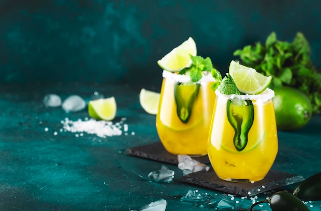 Cocktail margarita avec tequila jus de mangue piment jalapeno citron vert et sel fond bleu