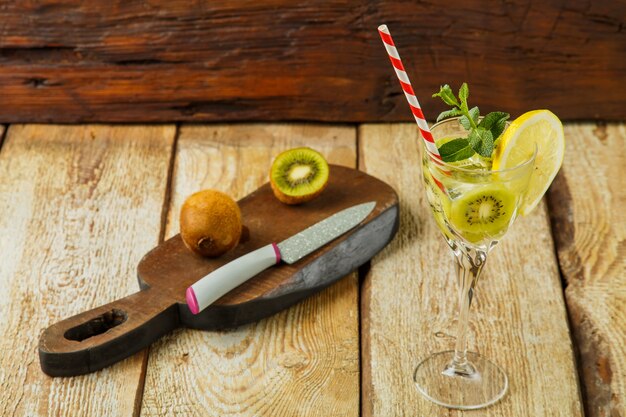 Cocktail à la menthe kiwi et au citron dans un verre sur une table en bois à côté du citron et du kiwi sur une planche. photo horizontale